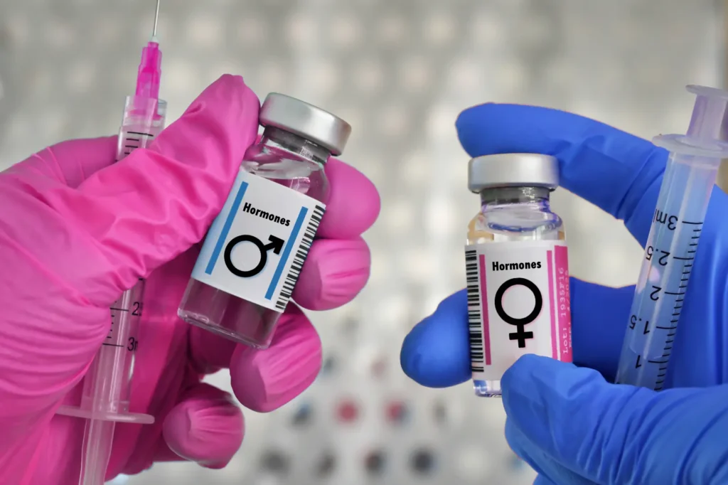Gloved hands hold hormone medication vials with male and female symbols alongside syringes.