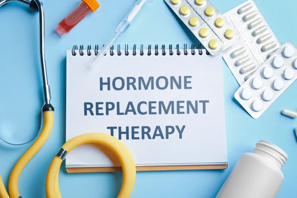 Notepad labeled hormone replacement therapy beside a stethoscope, syringe, blood sample tube, and medication packs.